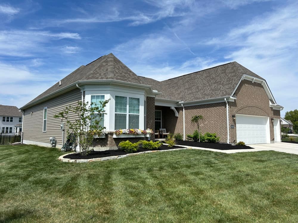Modern brick home with landscaped yard, flower beds, and clear blue sky. Perfect curb appeal.