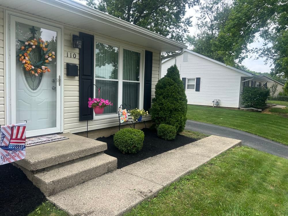 Front porch with decorative wreath, colorful flowers, and well-maintained landscaping.