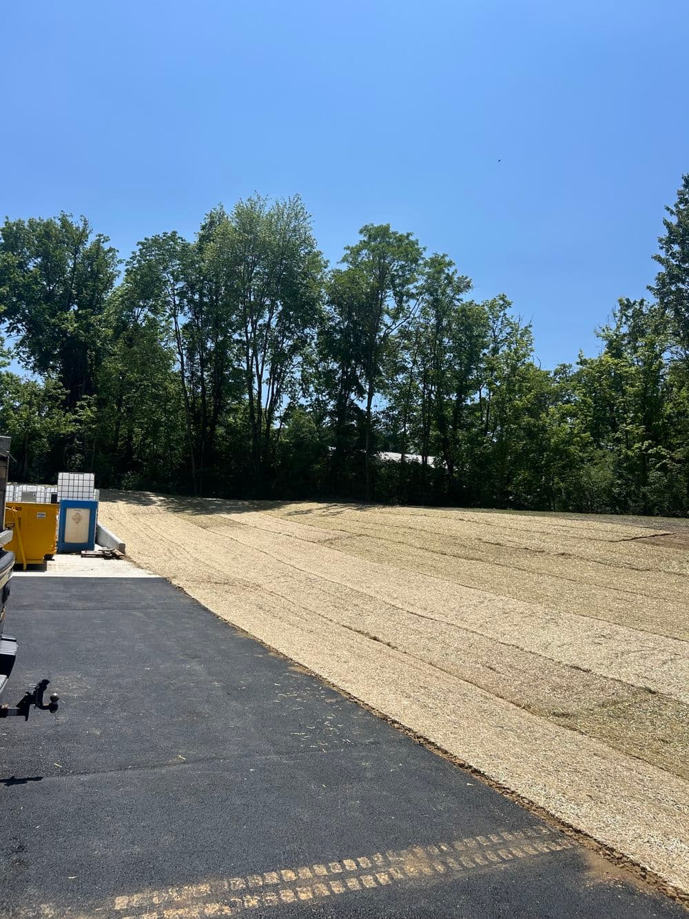 Vacant gravel lot with trees and blue sky, ideal for construction or landscaping projects.