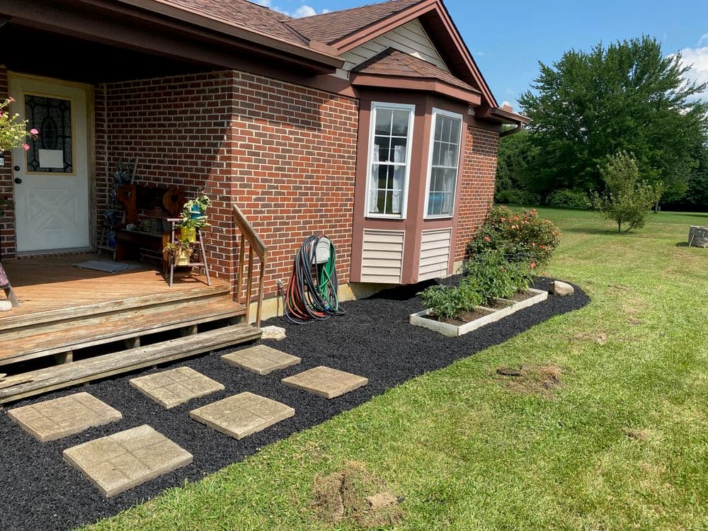 Front yard of a brick house featuring a garden, stone pathway, and black mulch landscaping.