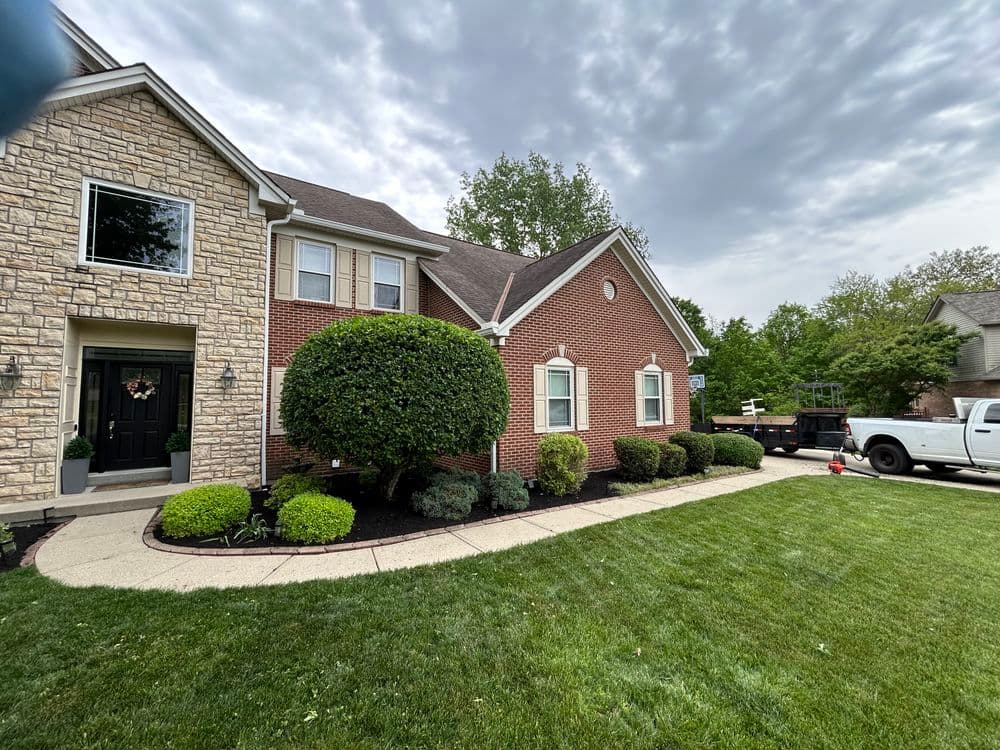 Brick home with landscaped yard, shrubs, and a work truck nearby under a cloudy sky.