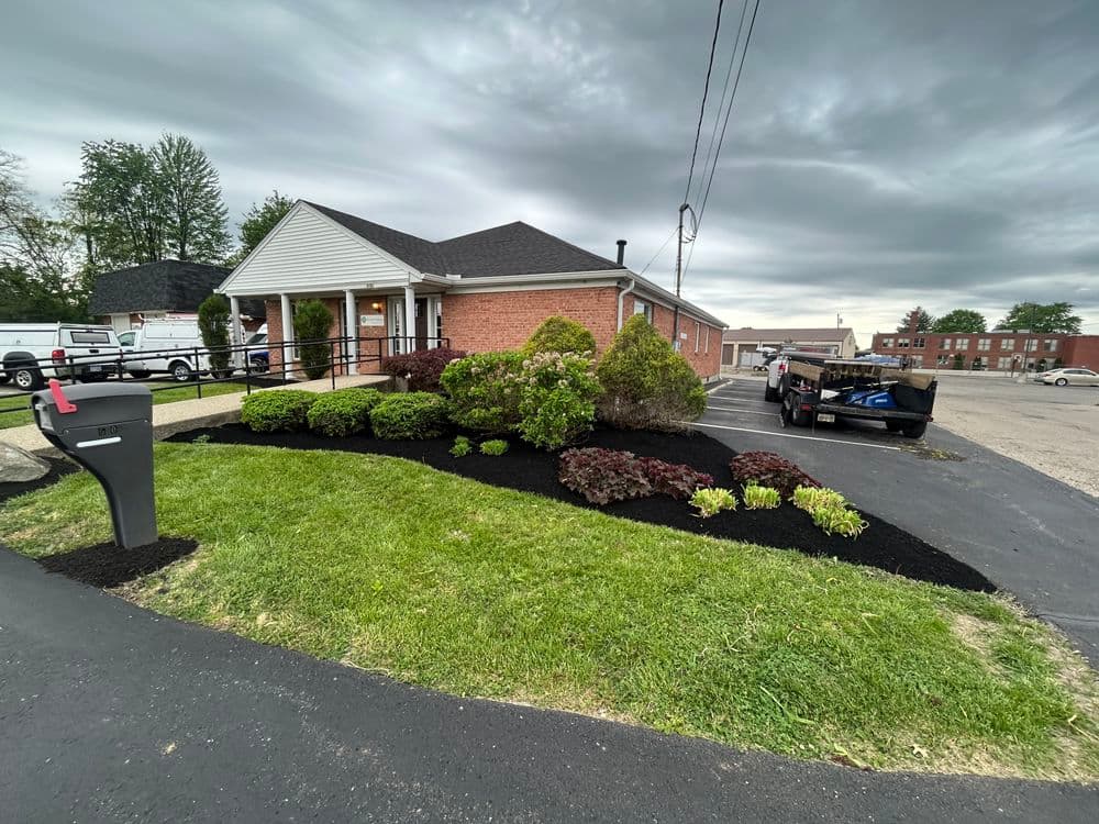 Landscaped office building with lush greenery and fresh mulch, set under a cloudy sky.