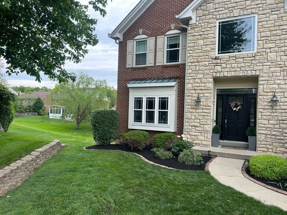 Elegant brick and stone house with manicured lawn and landscaped entrance.