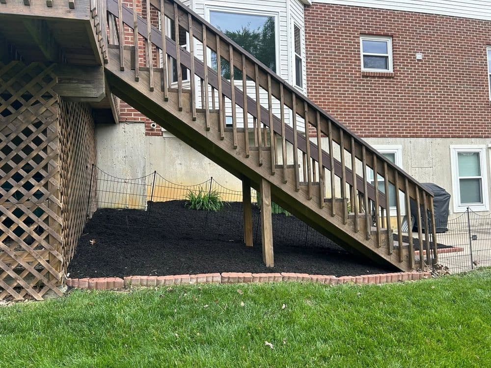 Wooden staircase leading to a backyard with mulch and green grass under a house.