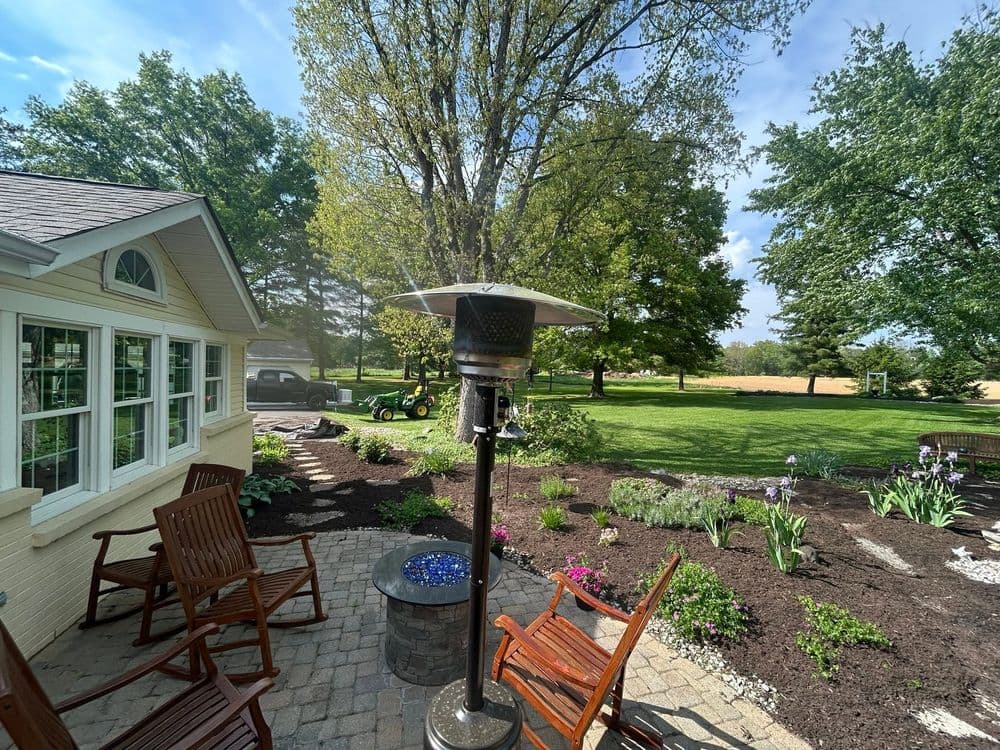 Patio with heater, flower beds, and green lawn in a serene outdoor setting.