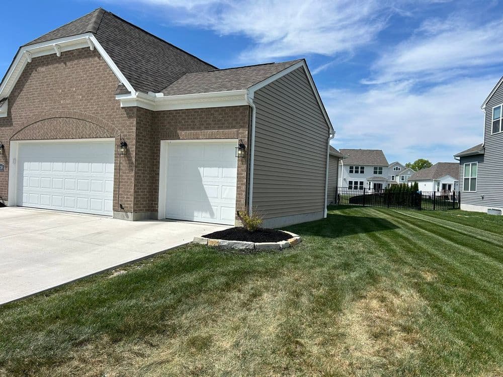 Newly built suburban home exterior with garages, manicured lawn, and clear blue sky.