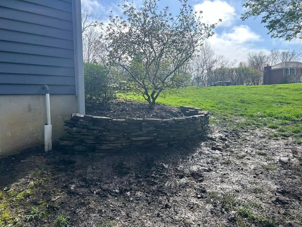 Stone planter bed with a flowering tree, surrounded by a grassy area and blue sky.